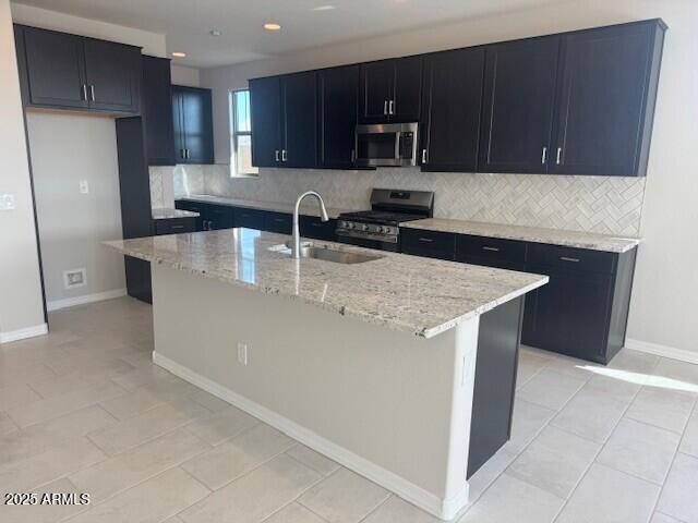 kitchen with stainless steel appliances, backsplash, a sink, and light stone countertops