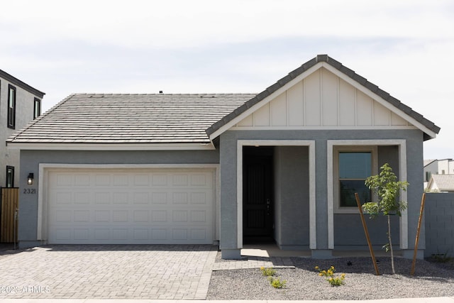 single story home with board and batten siding, decorative driveway, a tiled roof, and a garage
