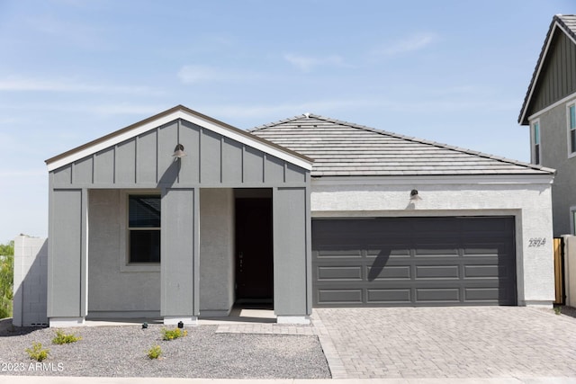 contemporary home with a garage, board and batten siding, a tiled roof, and decorative driveway