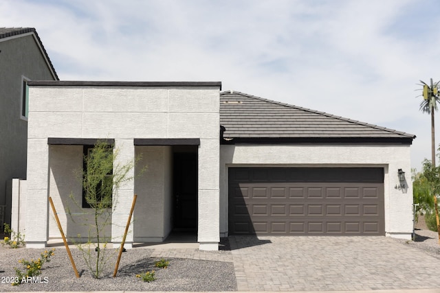 contemporary house featuring stucco siding, an attached garage, a tile roof, and decorative driveway