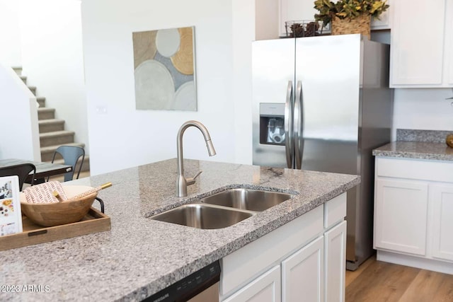 kitchen with a sink, stainless steel fridge with ice dispenser, white cabinets, and light stone counters