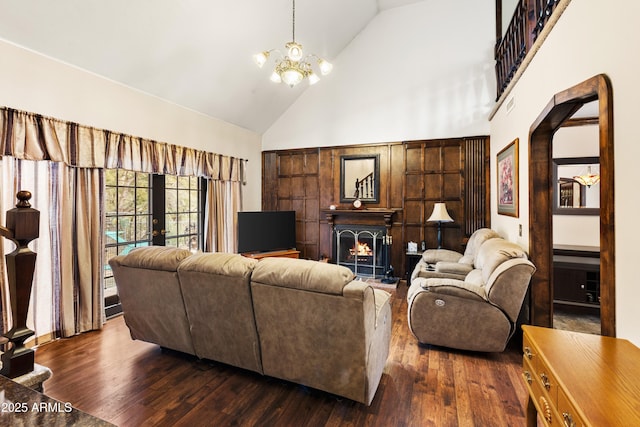 living room featuring french doors, an inviting chandelier, high vaulted ceiling, dark wood-type flooring, and a warm lit fireplace