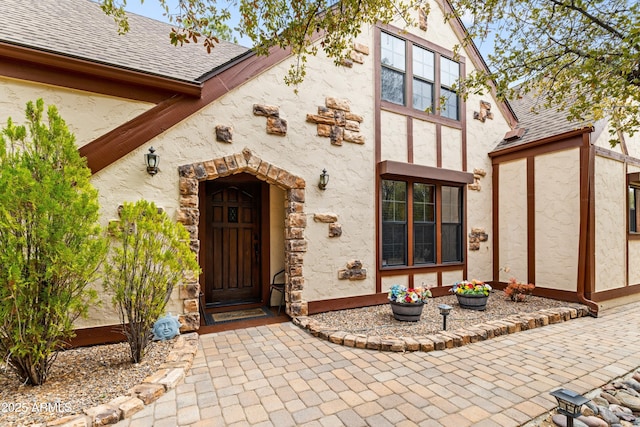 property entrance with stucco siding and roof with shingles
