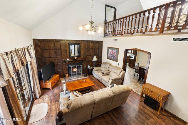 living area with high vaulted ceiling, visible vents, a warm lit fireplace, a notable chandelier, and wood finished floors