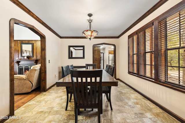 dining room with ornamental molding, arched walkways, stone finish flooring, and baseboards