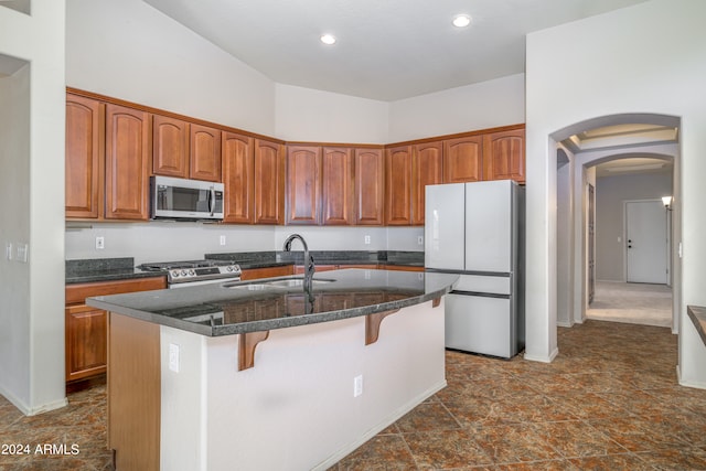 kitchen with arched walkways, appliances with stainless steel finishes, a sink, an island with sink, and a kitchen breakfast bar