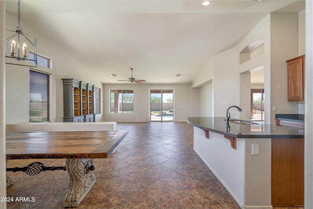 kitchen featuring baseboards, a kitchen breakfast bar, pendant lighting, a sink, and ceiling fan with notable chandelier