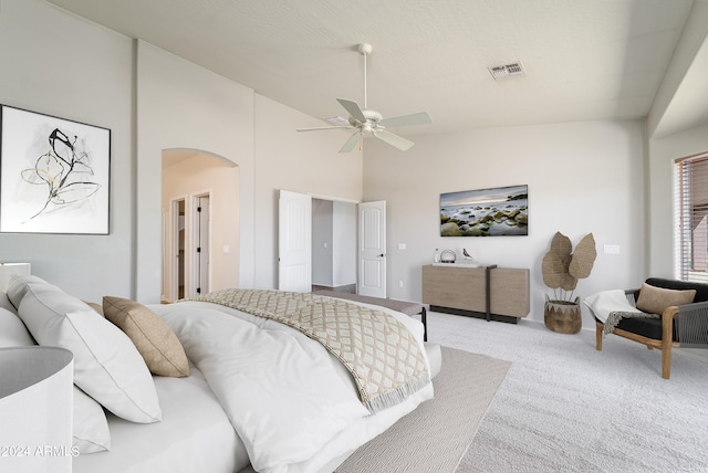 carpeted bedroom with high vaulted ceiling, arched walkways, visible vents, and ceiling fan