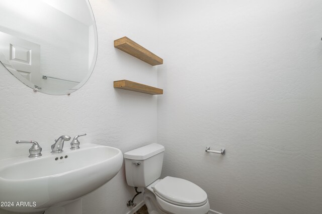 half bath with toilet, a sink, and a textured wall