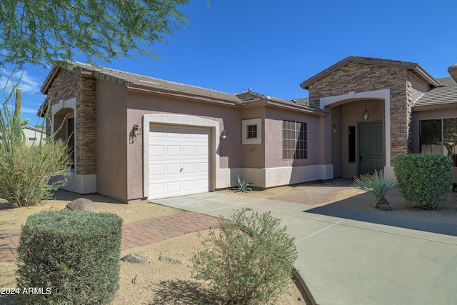 ranch-style house with stone siding, an attached garage, driveway, and stucco siding