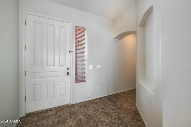 entryway featuring arched walkways, stone finish flooring, and baseboards