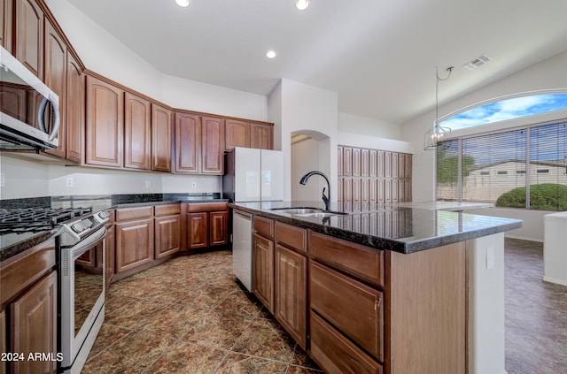 kitchen with hanging light fixtures, appliances with stainless steel finishes, a sink, an island with sink, and dark stone countertops