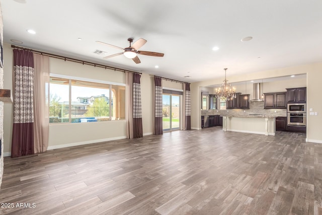 unfurnished living room featuring ceiling fan with notable chandelier, visible vents, baseboards, and wood finished floors