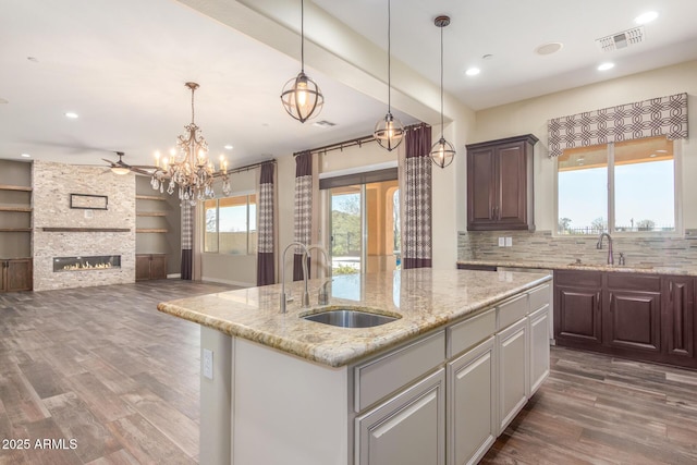 kitchen featuring visible vents, wood finished floors, a sink, and a stone fireplace