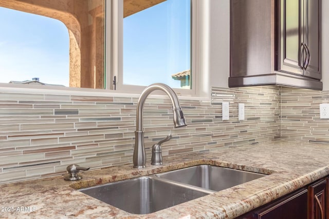 interior space with dark brown cabinets, light stone counters, decorative backsplash, and a sink