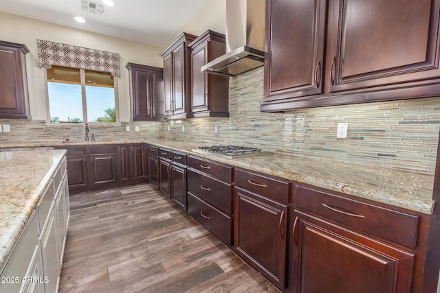 kitchen with wood finished floors, a sink, visible vents, decorative backsplash, and wall chimney exhaust hood