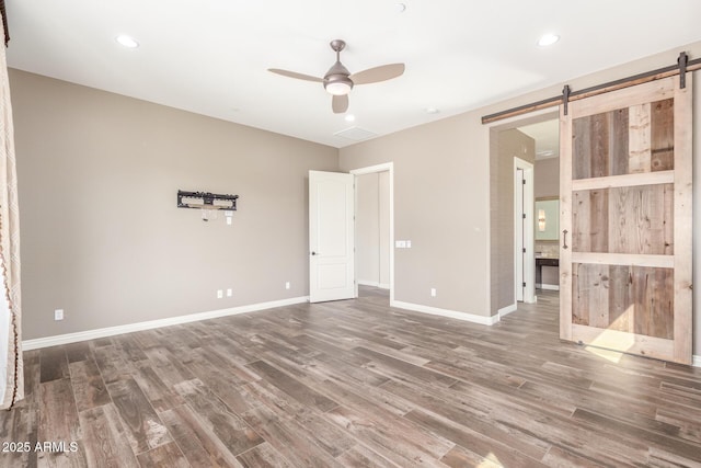 unfurnished room with a barn door, recessed lighting, wood finished floors, a ceiling fan, and baseboards