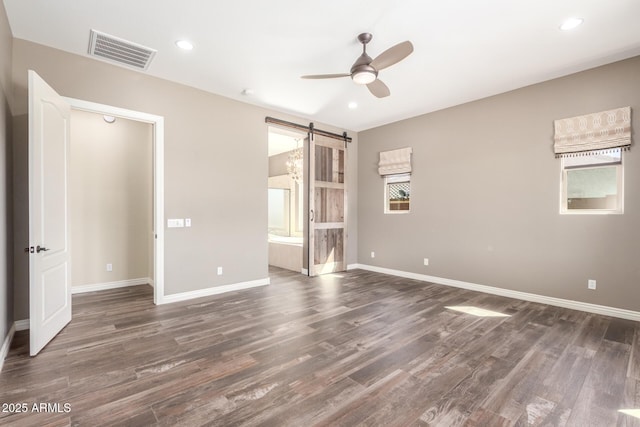 unfurnished bedroom with a barn door, wood finished floors, visible vents, and baseboards