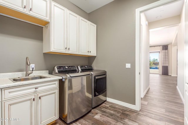 laundry room with dark wood-style floors, cabinet space, washing machine and dryer, a sink, and baseboards