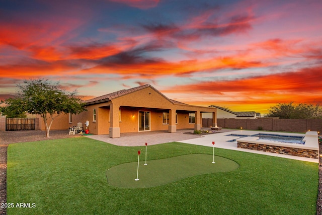 back of house at dusk with a fenced backyard, an in ground hot tub, a lawn, stucco siding, and a patio area