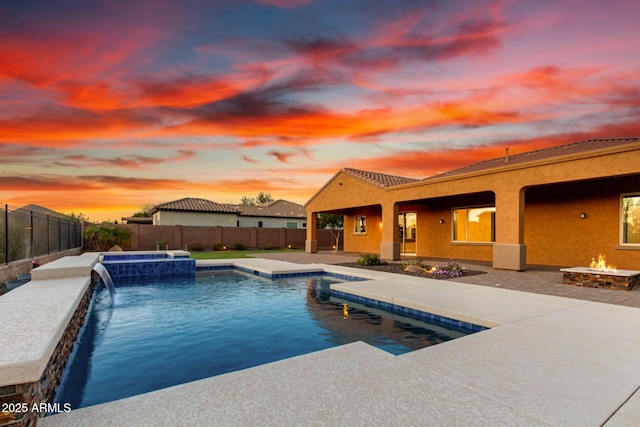 pool at dusk with an outdoor fire pit, a pool with connected hot tub, a fenced backyard, and a patio