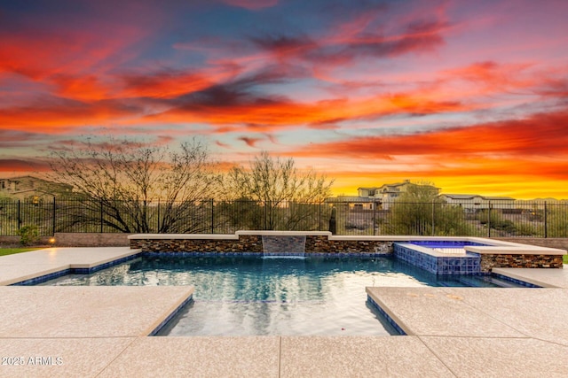 pool at dusk featuring a fenced backyard and a pool with connected hot tub