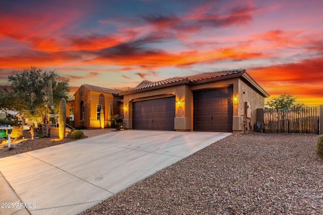 mediterranean / spanish-style house featuring stucco siding, fence, a garage, driveway, and a tiled roof