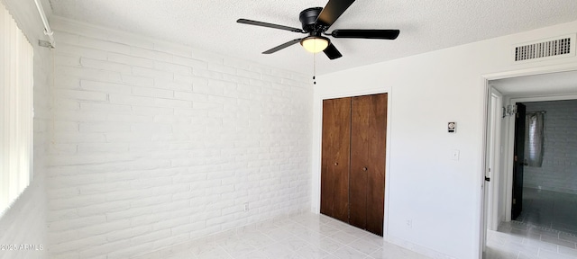 unfurnished bedroom featuring a textured ceiling, ceiling fan, brick wall, visible vents, and a closet