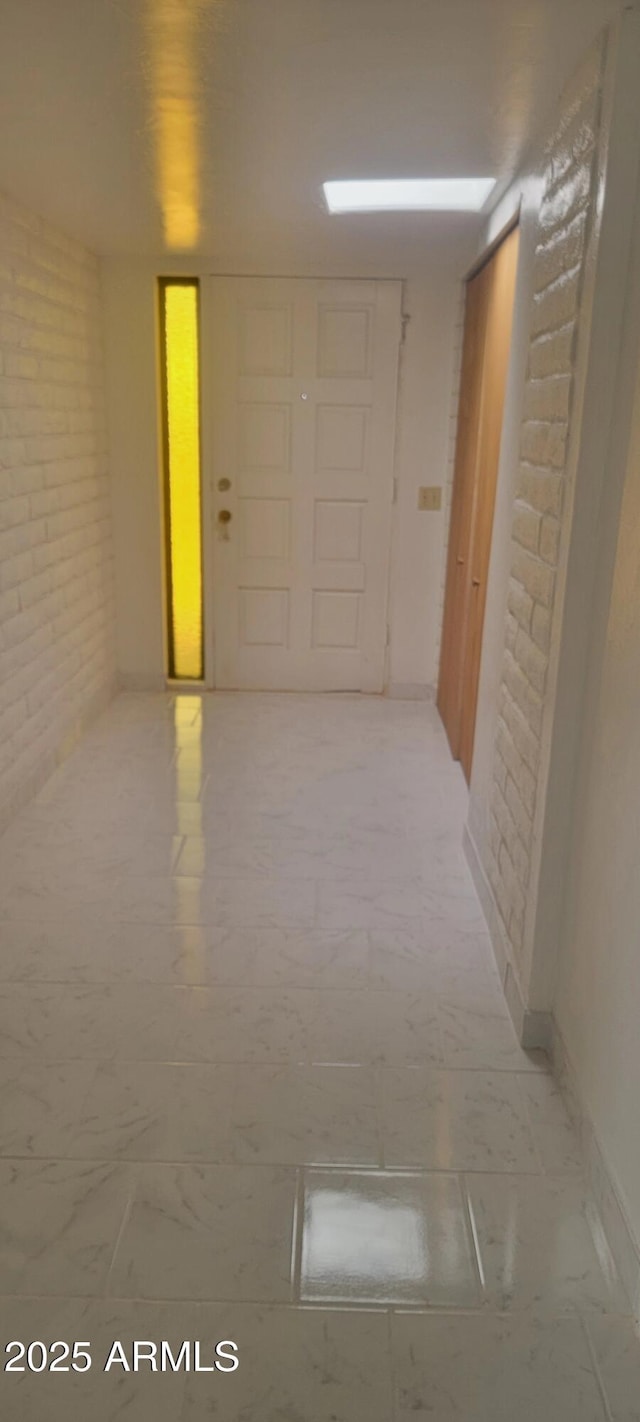 corridor with marble finish floor, brick wall, and baseboards