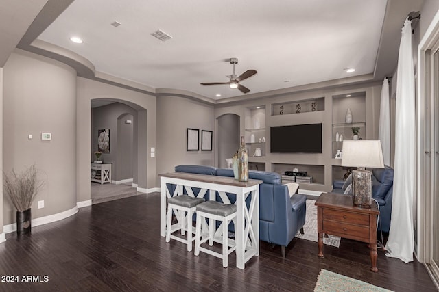 living room featuring built in shelves, ceiling fan, and dark hardwood / wood-style flooring