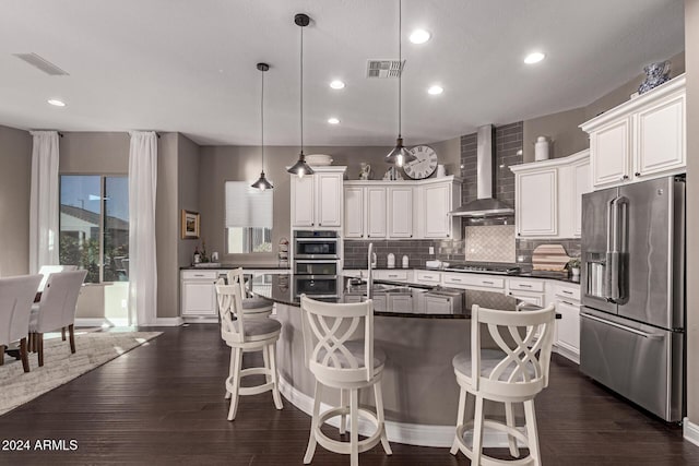 kitchen featuring a center island, wall chimney exhaust hood, stainless steel appliances, dark hardwood / wood-style flooring, and pendant lighting