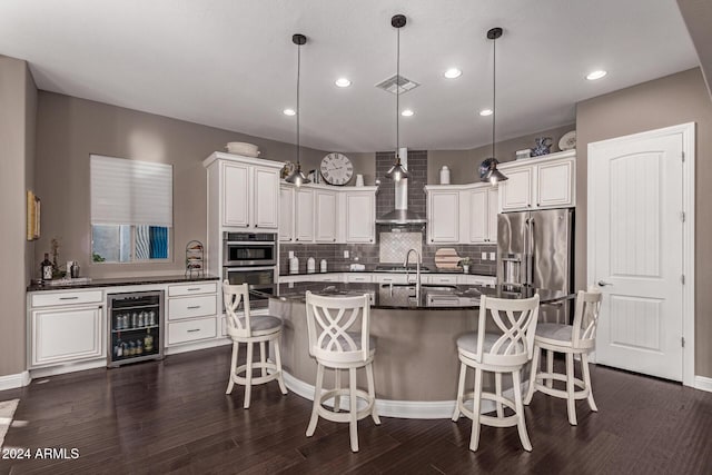 kitchen with decorative light fixtures, a center island with sink, beverage cooler, and wall chimney exhaust hood