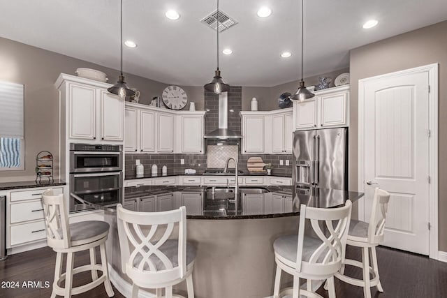 kitchen with pendant lighting, a center island with sink, wall chimney range hood, and stainless steel appliances