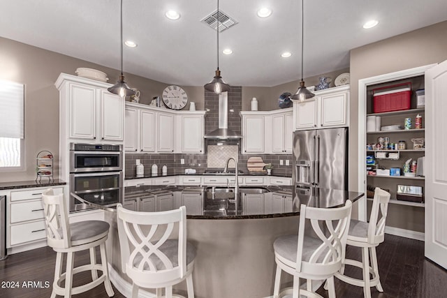 kitchen featuring pendant lighting, an island with sink, stainless steel appliances, and wall chimney range hood