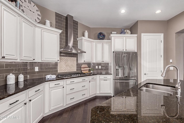 kitchen featuring appliances with stainless steel finishes, dark stone counters, wall chimney exhaust hood, sink, and white cabinets