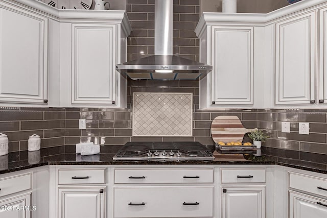 kitchen with white cabinets, tasteful backsplash, dark stone counters, and wall chimney range hood