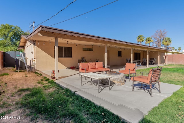 rear view of house with an outdoor living space with a fire pit, a patio area, fence, and concrete block siding