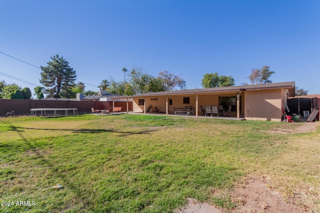 rear view of property featuring a trampoline, a yard, stucco siding, a patio area, and a fenced backyard