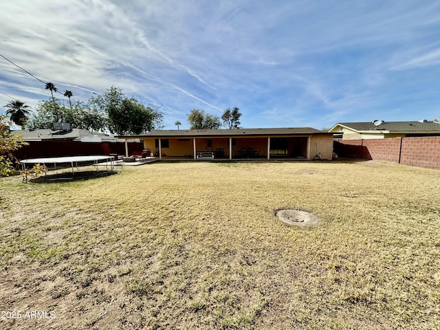 back of house featuring a trampoline, a yard, a fenced backyard, and a patio