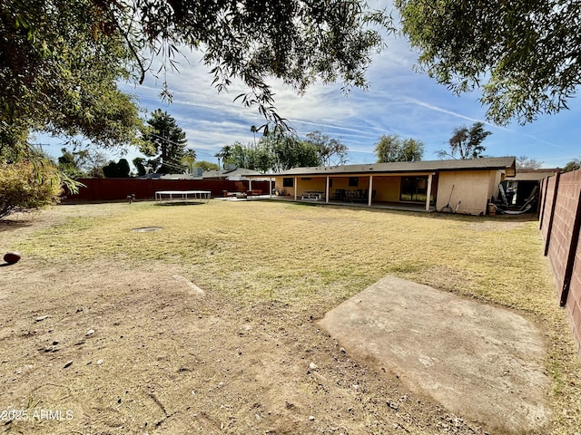 back of house featuring a trampoline, a patio area, fence, and stucco siding