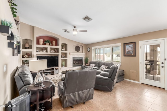 living area with light tile patterned floors, visible vents, ceiling fan, built in shelves, and a fireplace