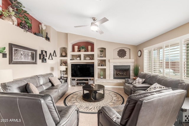 living room featuring built in shelves, light tile patterned flooring, ceiling fan, and a fireplace with raised hearth