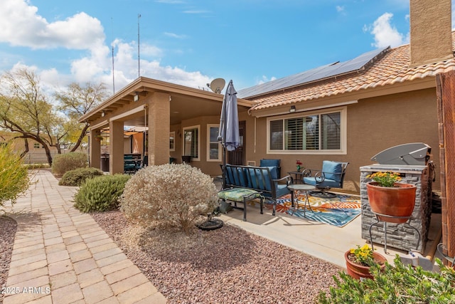 rear view of property with roof mounted solar panels, a patio, a tiled roof, and stucco siding