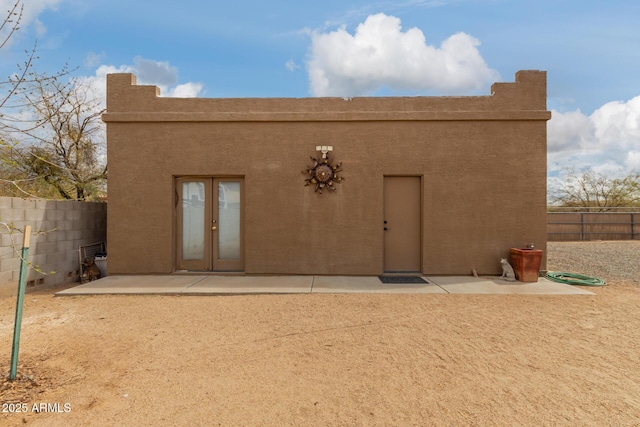 rear view of house with a patio area, fence, french doors, and stucco siding