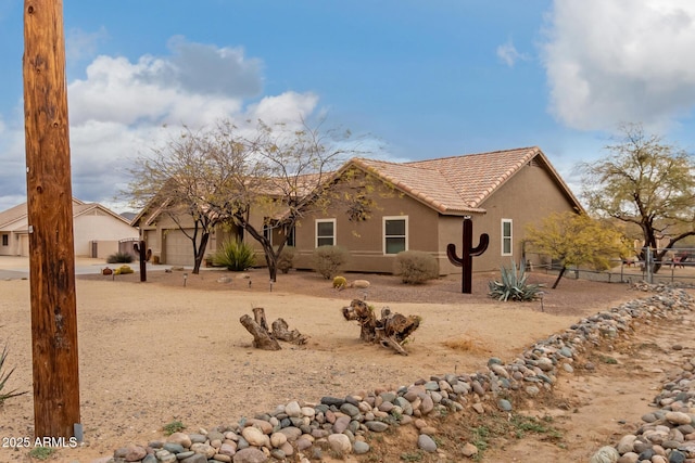 exterior space featuring fence, an attached garage, a tile roof, and stucco siding