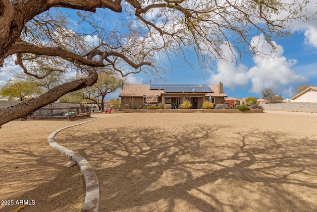 view of front of home featuring fence, a chimney, and solar panels