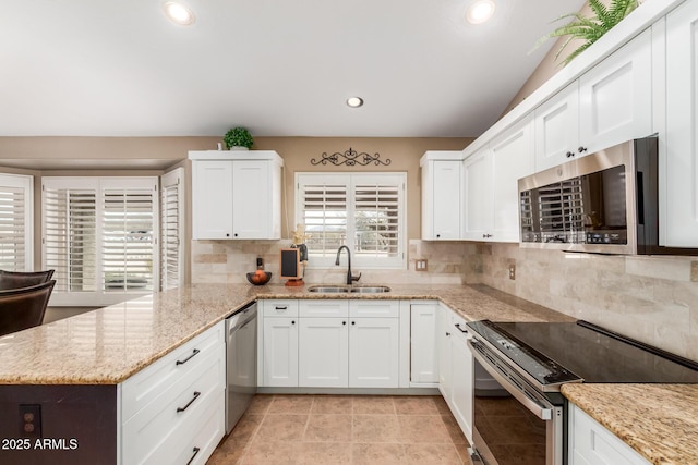 kitchen featuring appliances with stainless steel finishes, white cabinets, a sink, and a peninsula