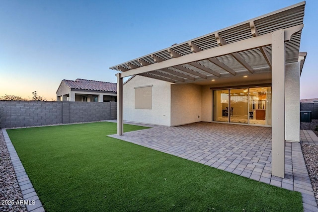 back house at dusk featuring a pergola, a patio area, and a lawn