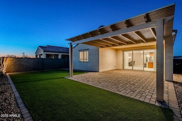 back house at dusk featuring a pergola, a lawn, and a patio