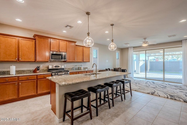 kitchen with pendant lighting, stainless steel appliances, sink, a kitchen island with sink, and ceiling fan